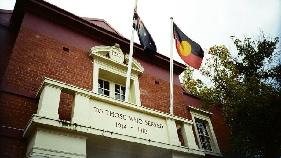 Image of the front of the Healesville Memorial Hall in Victoria, prominently displaying an Australian Flag and Aboriginal Flag. Engraved writing on the building says "To those who served 1914 - 1918".